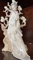 Full view of Lladro Geisha porcelain figurine sitting on a tree branch base, showing kimono and fan details.