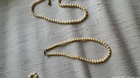 Two single strand pearl necklaces laid side by side showing round creamy white pearls and metal clasps.