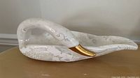 Side view of the white porcelain swan figurine showing gold beak and textured surface.