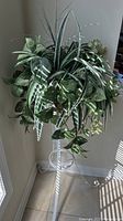 Faux fern plant with green and white variegated leaves atop white metal plant stand.