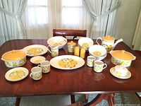 Full view of china set on table showing multiple pieces including covered casseroles, teapot, cups and plates with yellow floral design.