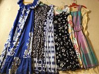 Six women's dresses hanging on hangers side by side, showing various patterns and colors including blue floral, black and white animal print, tie-dye, black floral, and pastel multicolor dresses.