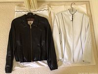 Black and white leather jackets laid flat on white fabric showing front and overall condition.