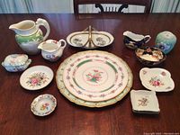 Full view of all pieces on wooden table including pitchers, divided serving dish, small bowls, square dishes, and lidded tureen.
