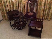 Four pieces of antique dark wood furniture and decor arranged on floor: one upholstered chair, wooden stand with spindles, two carved wall shelves.