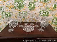 Set of six cut crystal wine glasses arranged in a row with three crystal bowls included, displayed on a wooden surface against a floral wallpaper background.
