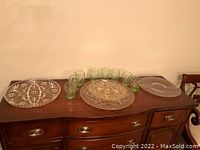 Photo of three large glass platters and six small green glasses arranged on wooden surface