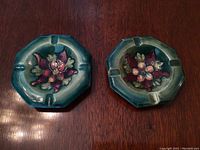 Pair of octagonal Moorcroft ceramic ashtrays with raised floral designs viewed from front on wood surface.