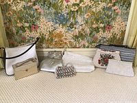Wide view showing all nine purses and clutches arranged on carpet with floral wallpaper background