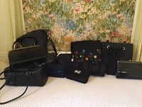 Wide shot of all purses and handbags in the lot showing two rows of seven items overall, mostly black bags with different styles and handles.