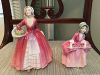 Front view of both porcelain Royal Doulton figurines: Bo Peep with basket of flowers, and Janet in pink dress.