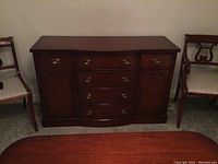 Front view of the wooden sideboard buffet showing the bowed center with three drawers and two cabinet doors on the sides, brass hardware, and warm medium brown wood finish.