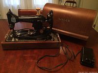 Singer sewing machine on wooden base with matching wooden carrying case and foot pedal on wooden table under natural light.