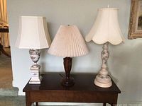 Three table lamps on a wooden console, different bases and shades visible.