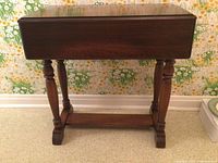 Side view of the wood drop-leaf table with leaves folded down, showing turned legs and stretcher base.