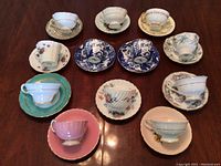 Overview of eleven assorted teacup and saucer sets on wooden table