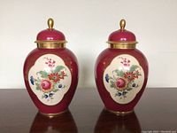 Pair of maroon porcelain vases with floral cream panels and gold trim, with lids on top.