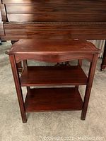 Front view of wood side table showing top surface and two lower shelves in dark brown finish with curved apron detail.