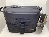 Front view of the LowePro ProTactic SH 200 AW camera bag with front flap closed showing clasp, black fabric, and attached tags.
