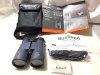 Binoculars and all included accessories laid out: case, cleaning cloth, neck strap, manuals.