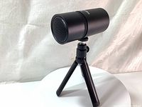 Front angled view of the black cylindrical Thronmax M8 Pulse USB microphone mounted on a black tripod stand, showing the microphone grille and tripod legs.