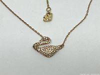 Close-up image of the swan-shaped pendant encrusted with clear crystals and the rose gold rhodium plated chain detail with small swan charm near the clasp.