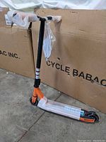 Side view of the Mongoose Rise 100 trick scooter showing the orange fork, black handlebar and partially wrapped in protective packaging.