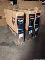 Three boxed Mongoose Rise 110 Team scooters stacked on a concrete floor, showing box condition varies with some corner damage.