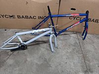 Two bicycle frames on concrete floor, one blue Giant BMX frame with front fork, and one white CCM frame