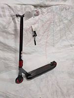 Full left side view of Mongoose Rise 100 trick scooter showing T-bar handle with grip wrap, deck, rear brake, and front wheel with peg.