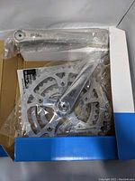 Shimano Deore triple crankset still in plastic wrapper inside original box showing crank arms and chainrings