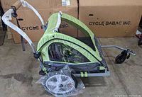 Side view of assembled green and gray trailer with handlebar, front wheel installed and rear wheels in plastic bag
