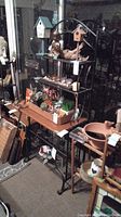Full view of wrought iron bakers rack loaded with various items (not included with sale). Rack has scrollwork design and single wood shelf in the middle.