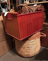 Rectangular reddish-brown wicker basket with cut-out handles sitting on top of a large round light tan seagrass or wicker basket.