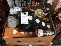 Top-down view of a box filled with assorted candles and candle holders including wooden holders with glass inserts, various sizes and shapes of candle holders.