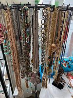 Wide view of six hooks filled with various costume jewelry necklaces including chains, beads, and pendants in different colors and materials.