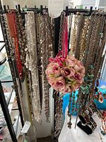 Front view of 6 hooks holding numerous costume jewelry necklaces in silver and gold metal chains, faux pearls, beads, and a hanging pink rose bouquet ornament.