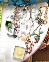 Full view of costume jewelry lot laid on table showing necklaces, some earrings and bracelets in several colors and styles including turquoise, pink, amber, neutral tones.