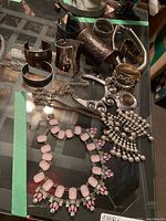 Photo of multiple metal arm cuffs and bracelets in silver and bronze tones with varying designs, displayed on a glass table.