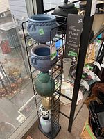 Metal stand displaying various ceramic pots and vases near a window
