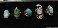 All five rings arranged side by side on a black background showing variety of gemstone colors and settings.