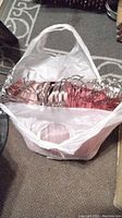 White bag filled with metal and plastic children's hangers on a patterned carpet.
