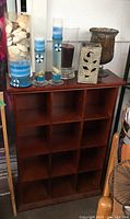 Wooden 12-cubby storage shelf with various decorative candles and vases on top, including tall and short nautical-themed candles and shell-filled vase.