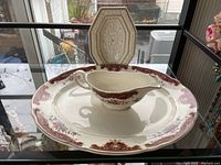 Photo showing large round plato with red and gold floral pattern and a porcelain gravy boat with floral decoration inside it