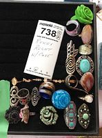 Photo of 26 assorted rings and black display case showing varied designs and colors.