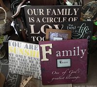Six word art wall decorations and photo frames arranged on floor including large purple 'Family' piece with photo frame, black and white inspirational quotes, and two separate photo frames.