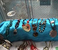 Overview of nine necklaces and bracelets arranged on blue fabric covering a rolled display. Varied stone and pendant styles visible.