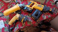 Yellow and black Dewalt cordless reciprocating saw, battery pack, charger, yellow and black corded drill and angle grinder on patterned cloth surface