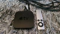 Apple TV device and silver Apple remote on grey carpet