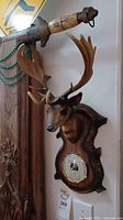 Full view of the resin deer head with mounted barometer on faux wood plaque hanging on wall.